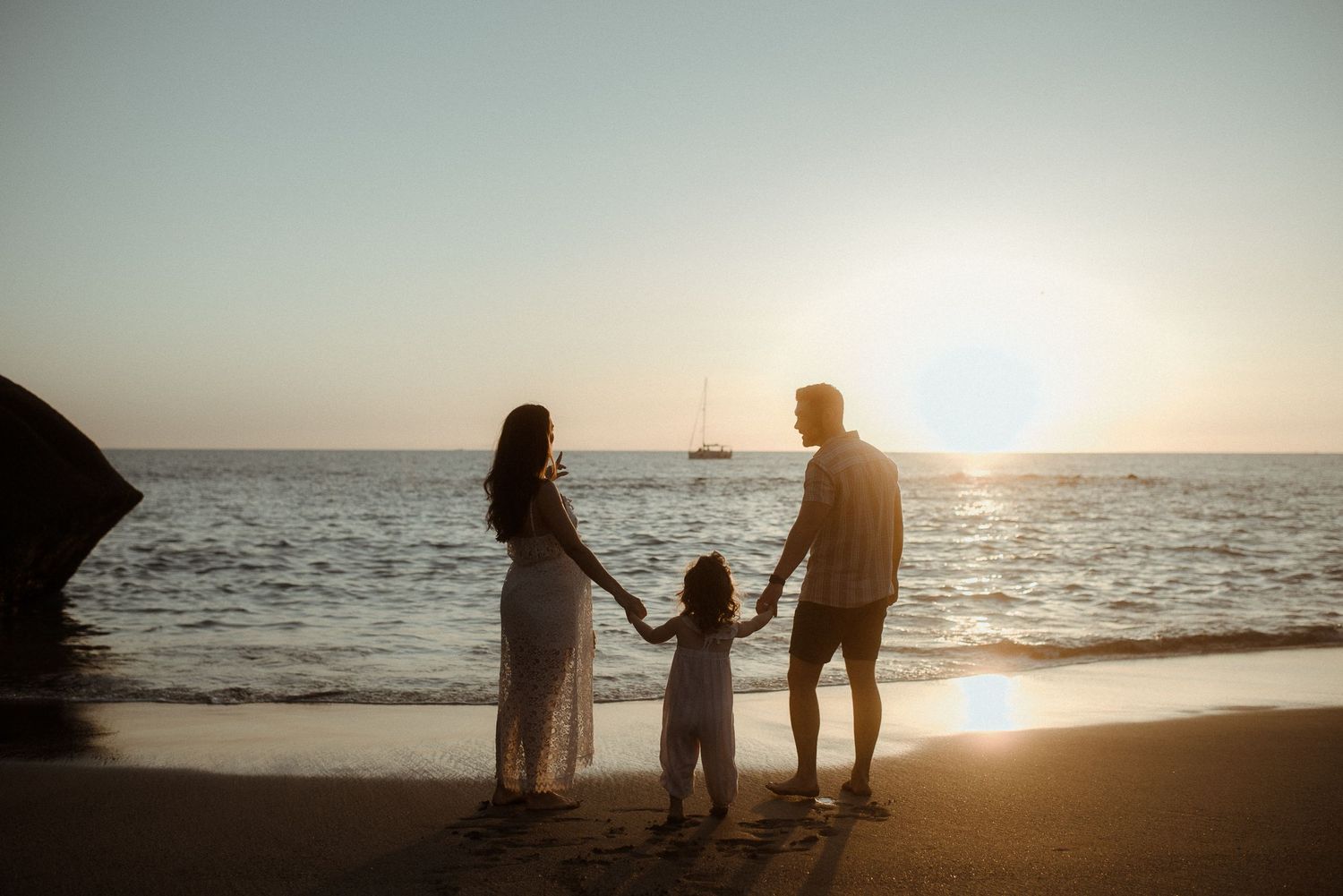 A family holds hands while watching sunset on a beach with rocky outcrops. Tenerife Wedding Photographer at Playa del Duque, Adeje.