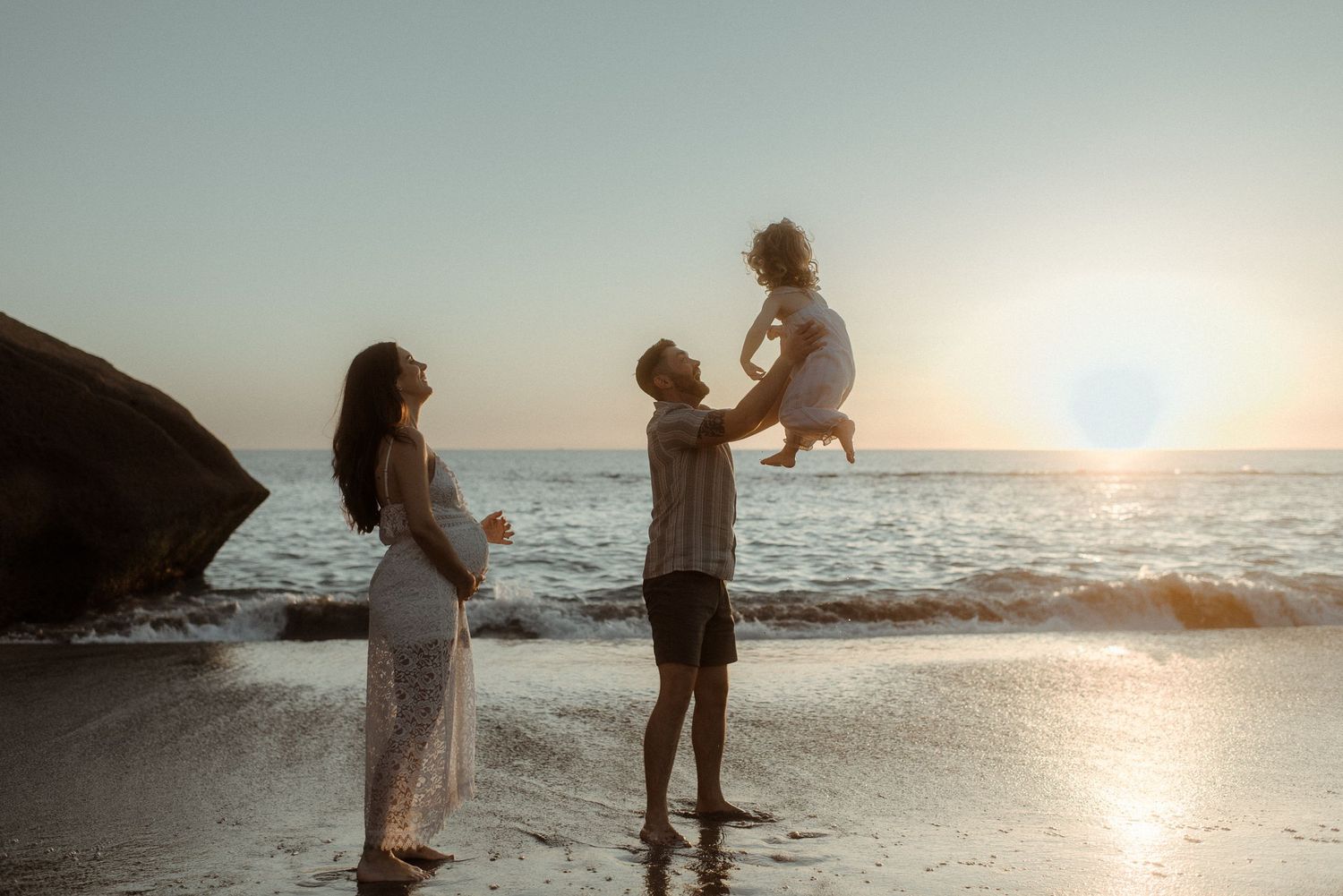 A family plays together on a beach at sunset near large rocks. Tenerife Wedding Photographer at Playa del Duque, Adeje.