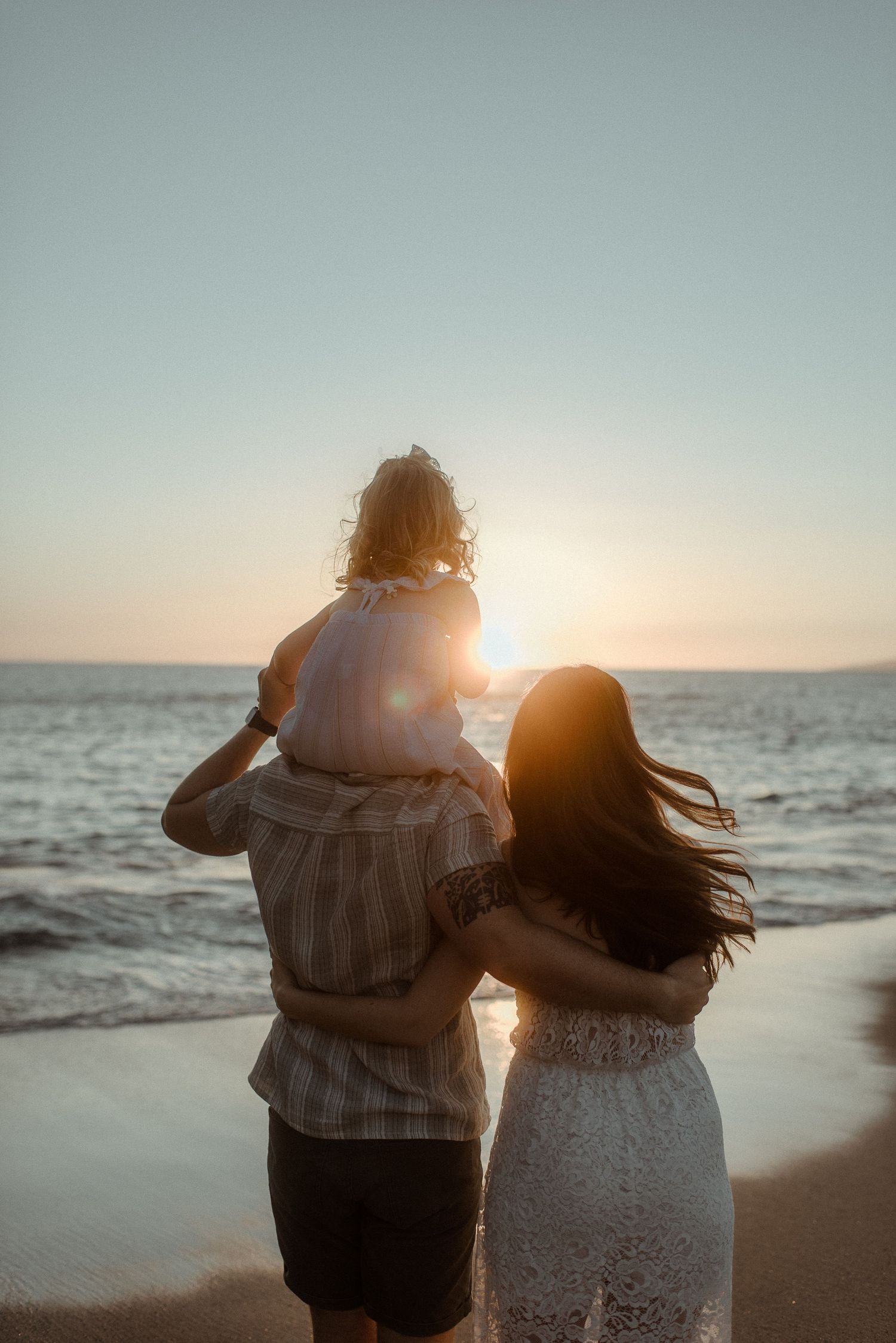 A family watches the ocean sunset together on a peaceful beach. Tenerife Wedding Photographer at Playa del Duque, Adeje.