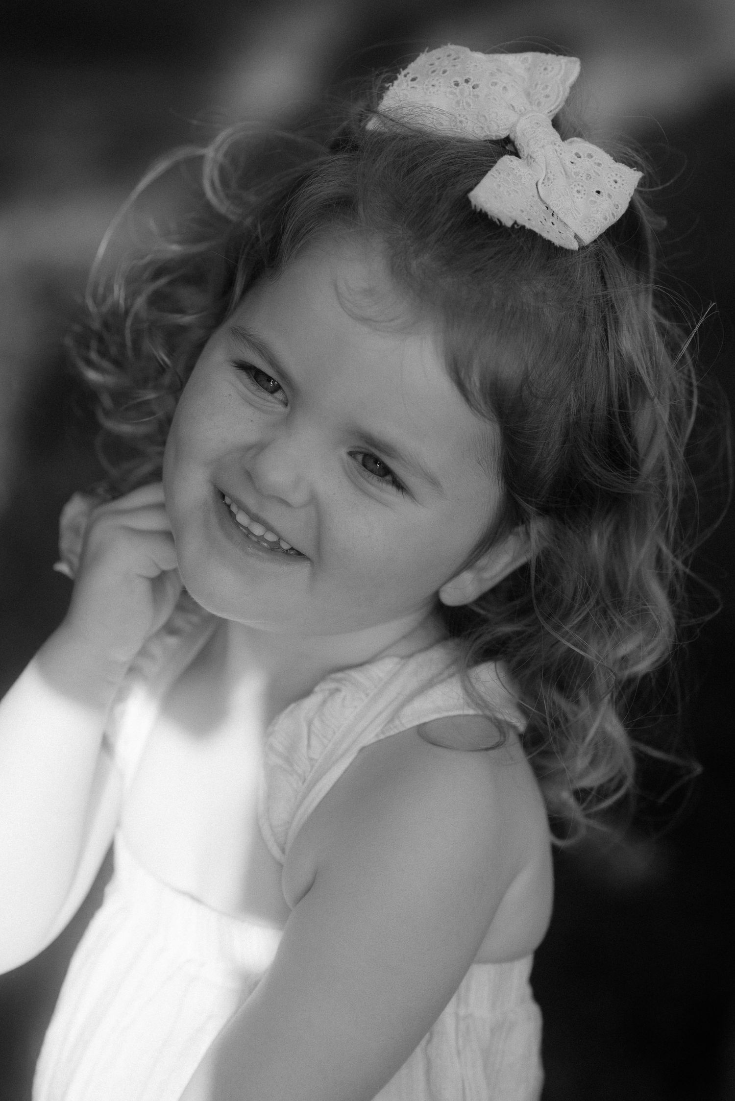 A young child in a white dress smiles brightly while wearing a decorative bow in their curly hair. Tenerife Wedding Photographer