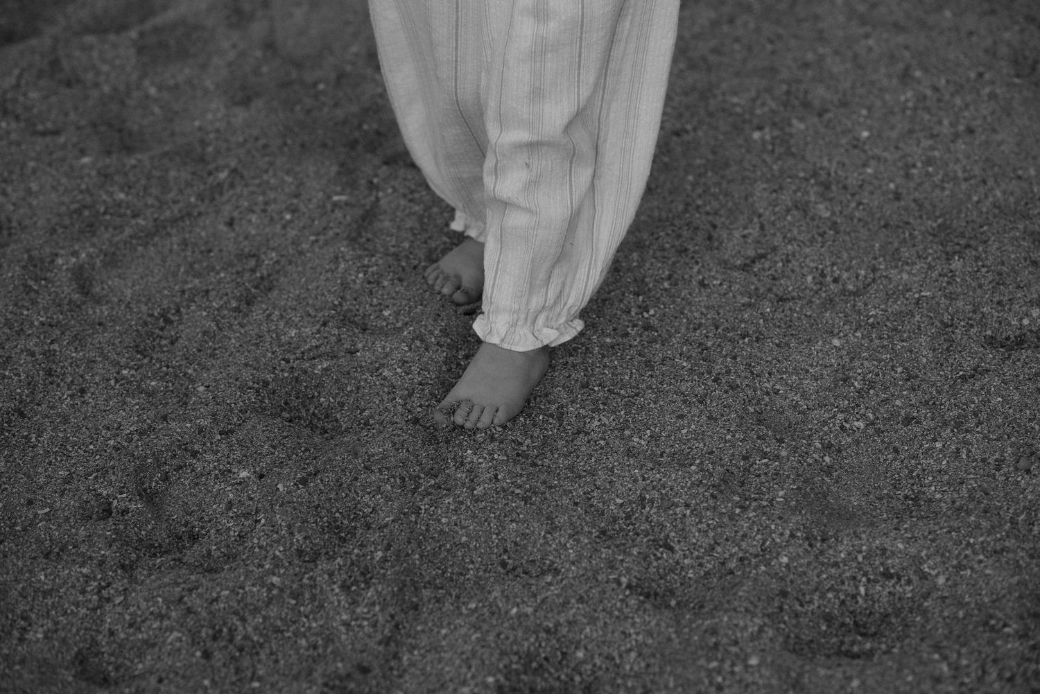 Black and white photo of bare feet on sand wearing a flowing white dress. Tenerife Wedding Photographer at Playa del Duque, Adeje.
