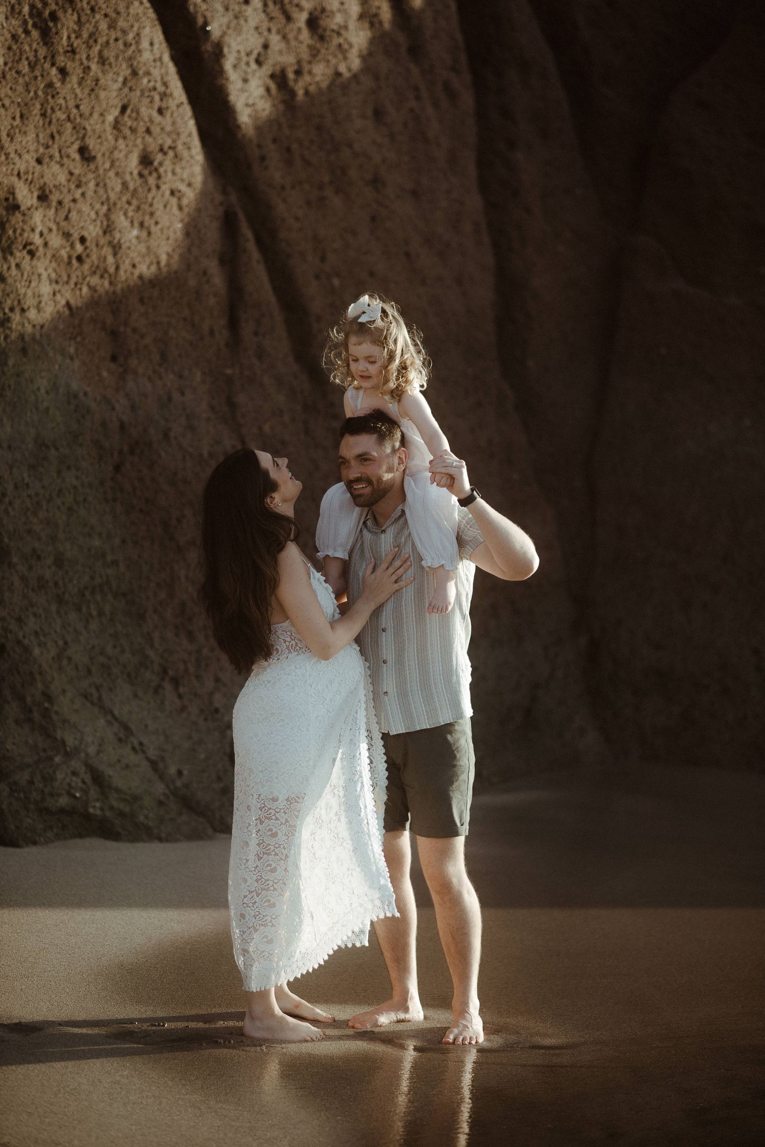 A family shares intimate moments together by rocky coastal formations. Tenerife Wedding Photographer at Playa del Duque, Adeje.