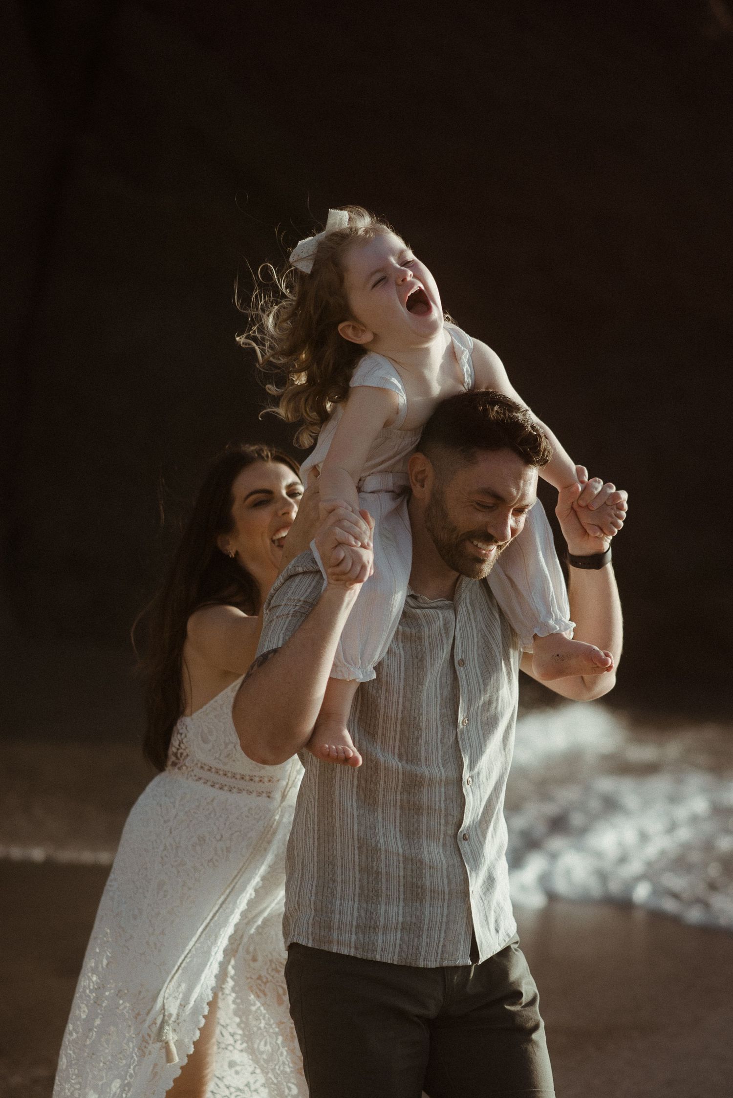 Joyful family moment captured on beach with child being lifted up. Tenerife Wedding Photographer at Playa del Duque, Adeje.