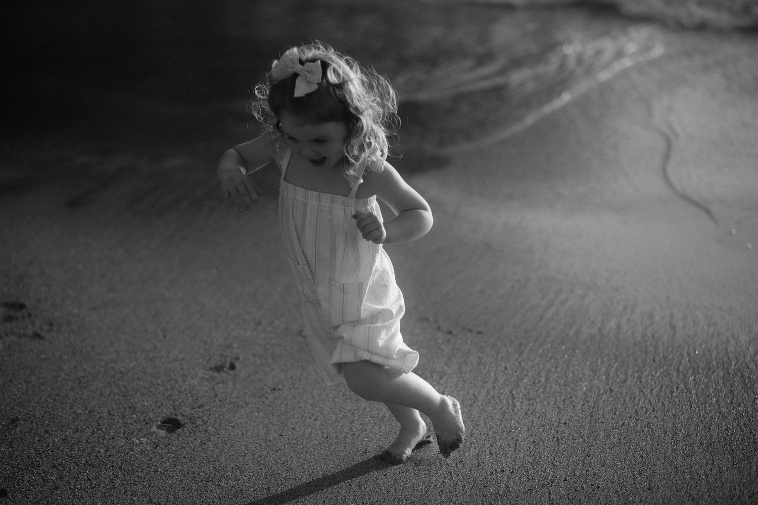 Black and white photo of child jumping and playing on beach sand. Tenerife Wedding Photographer at Playa del Duque, Adeje.