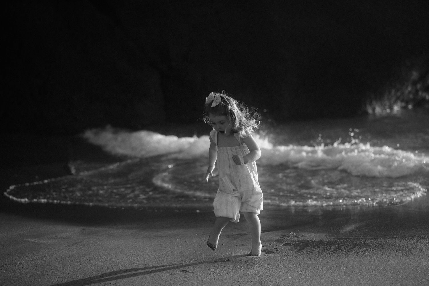 Black and white image of child dancing by ocean waves. Tenerife Wedding Photographer at Playa del Duque, Adeje.