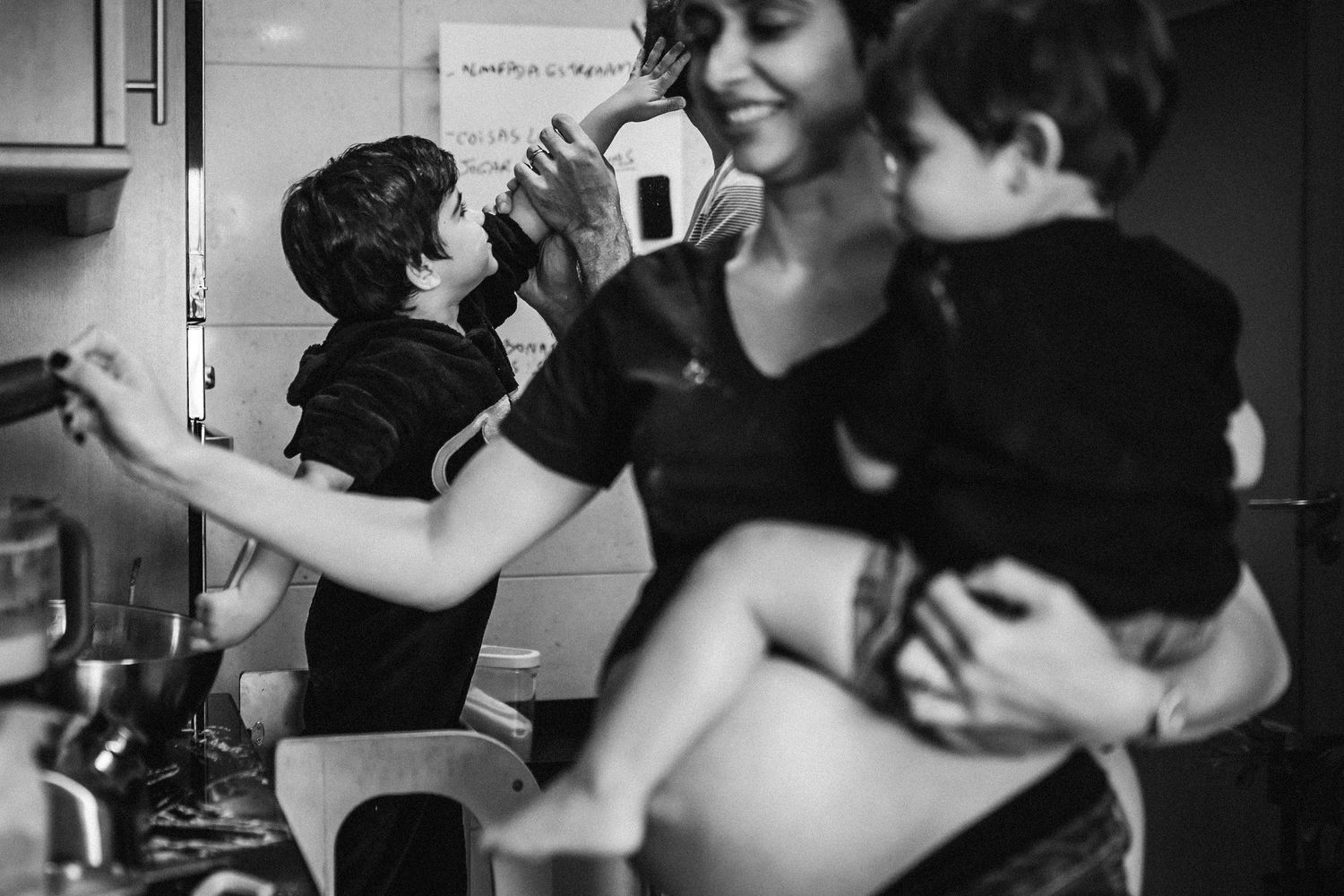 A candid black and white moment in a kitchen shows people gathered together in a relaxed domestic scene.