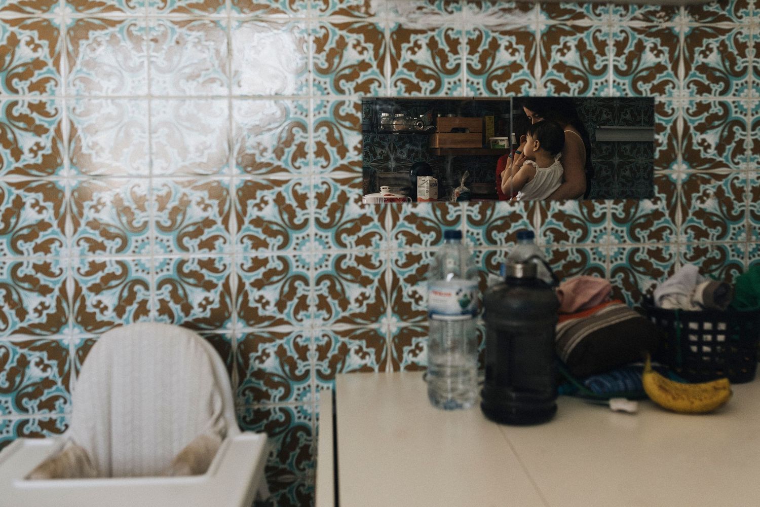 A modern kitchen interior with ornate blue and white patterned tile backsplash and a black kettle on the counter.