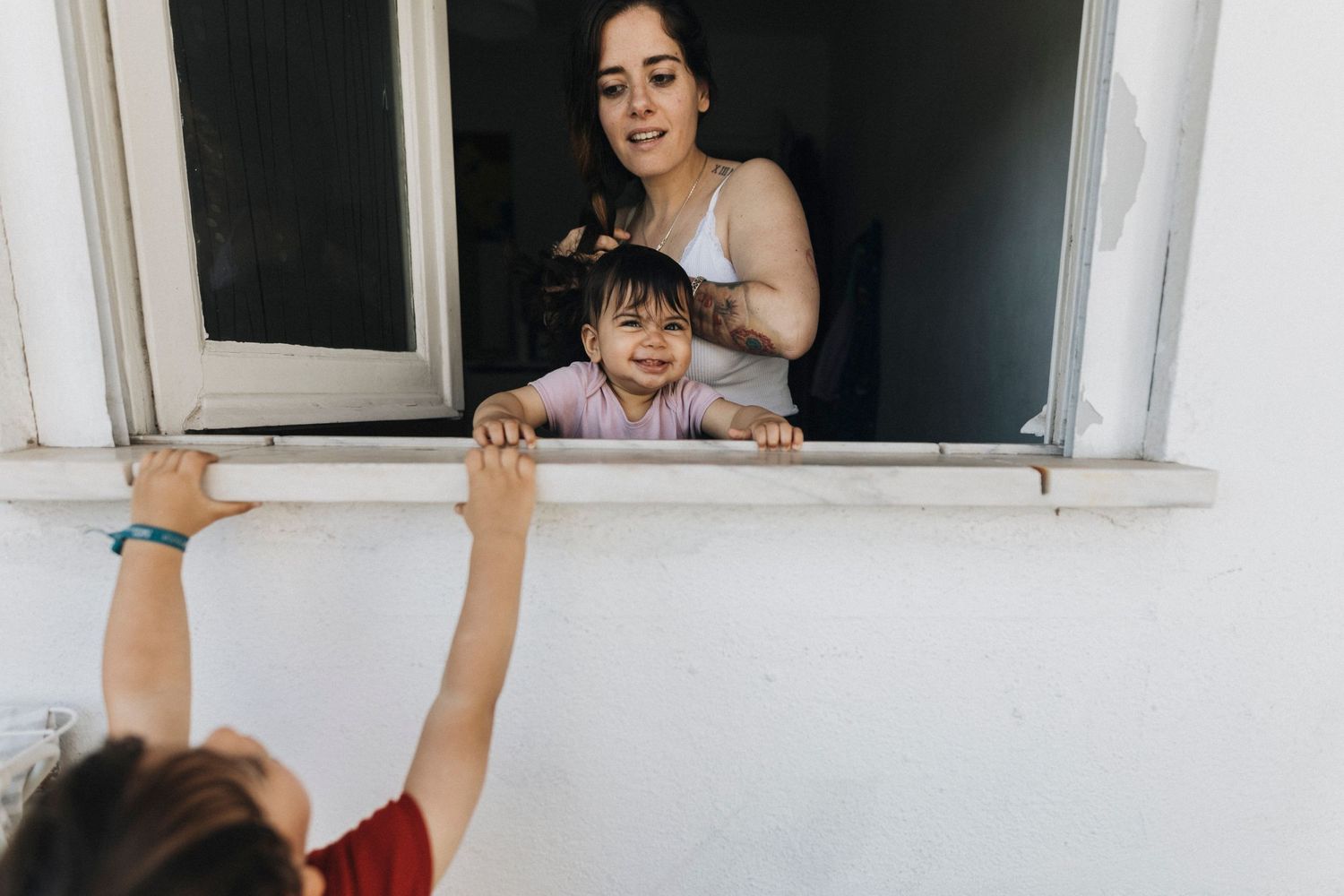 A happy family moment captured through a window as two people interact playfully from inside and outside the house.