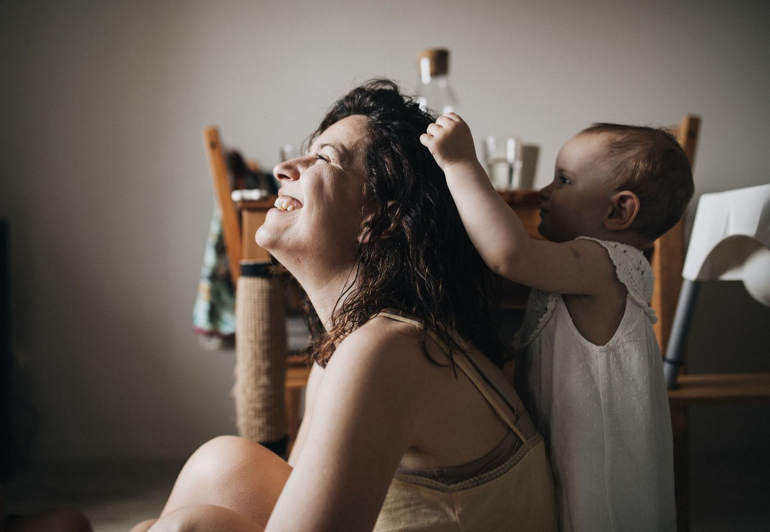 Two people share an intimate bonding moment as one gently styles the others wet long dark hair in a dimly lit room.