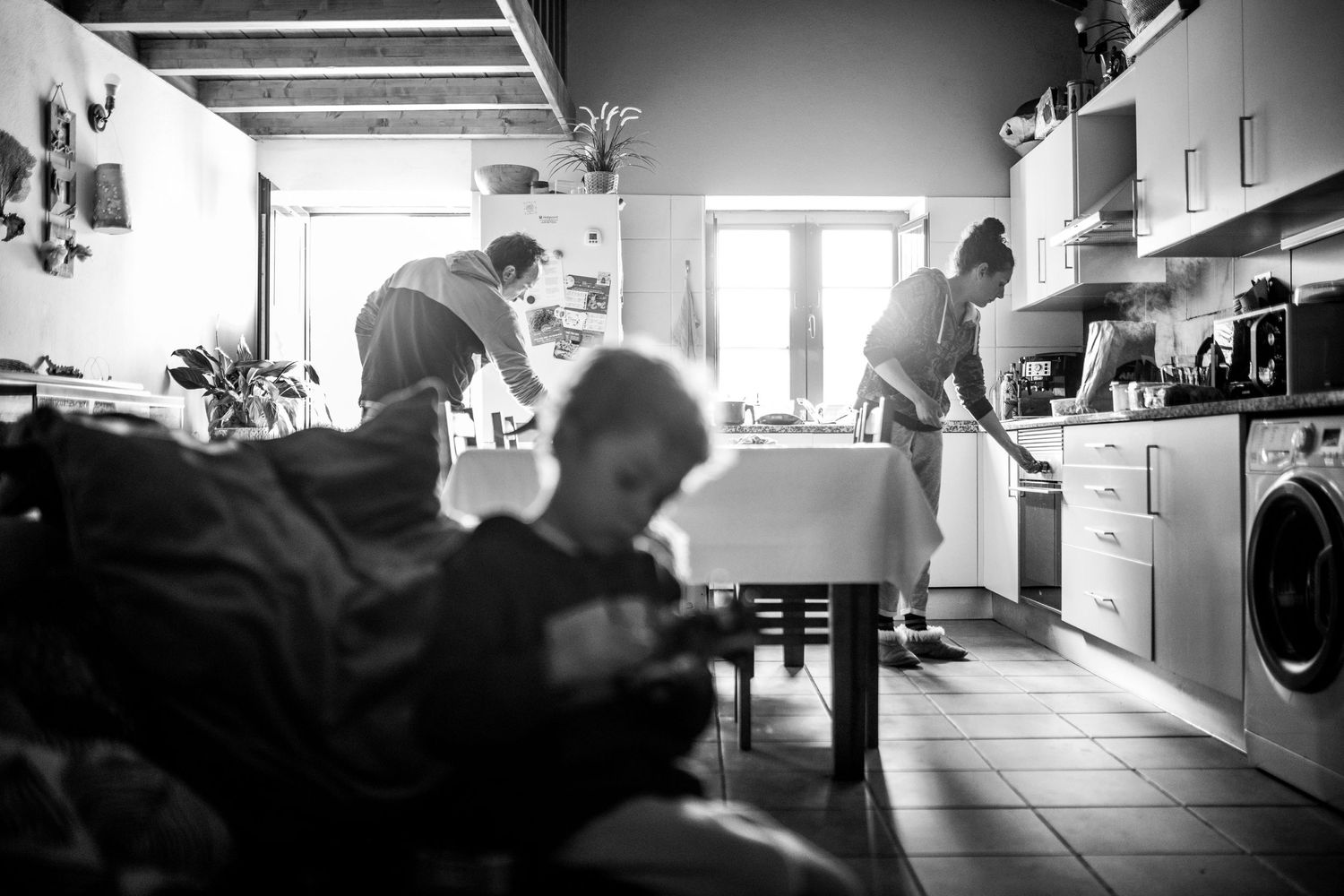 People working in a communal kitchen space with sunlight streaming through windows while preparing food.
