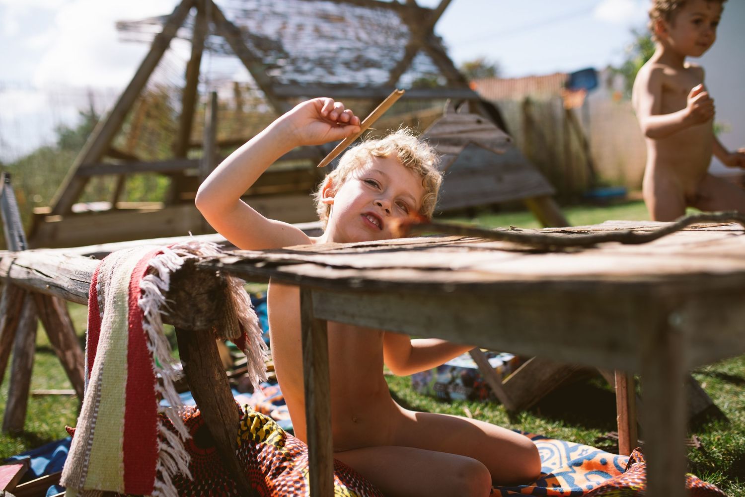 A family enjoys a warm summer day relaxing outdoors on wooden lawn furniture in dappled sunlight.