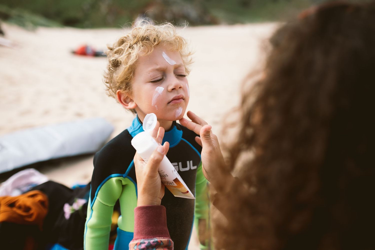 A small child gets their cheeks wiped with a napkin by someone off-frame during an outdoor meal.