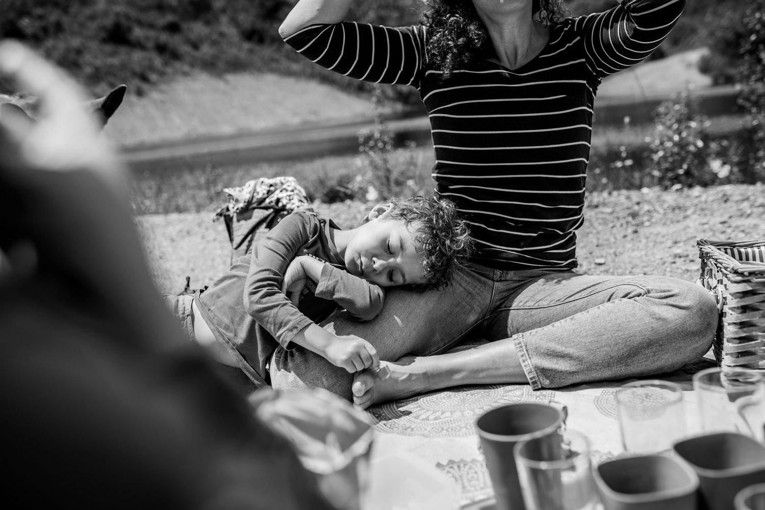 A candid black and white shot of people relaxing outdoors on a picnic blanket with drinks and snacks.