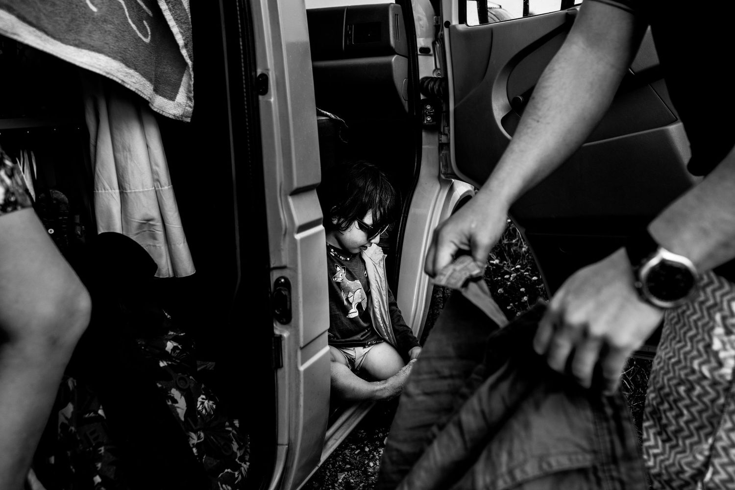 Black and white shot showing hands and legs of multiple people sitting inside a crowded public transit vehicle.