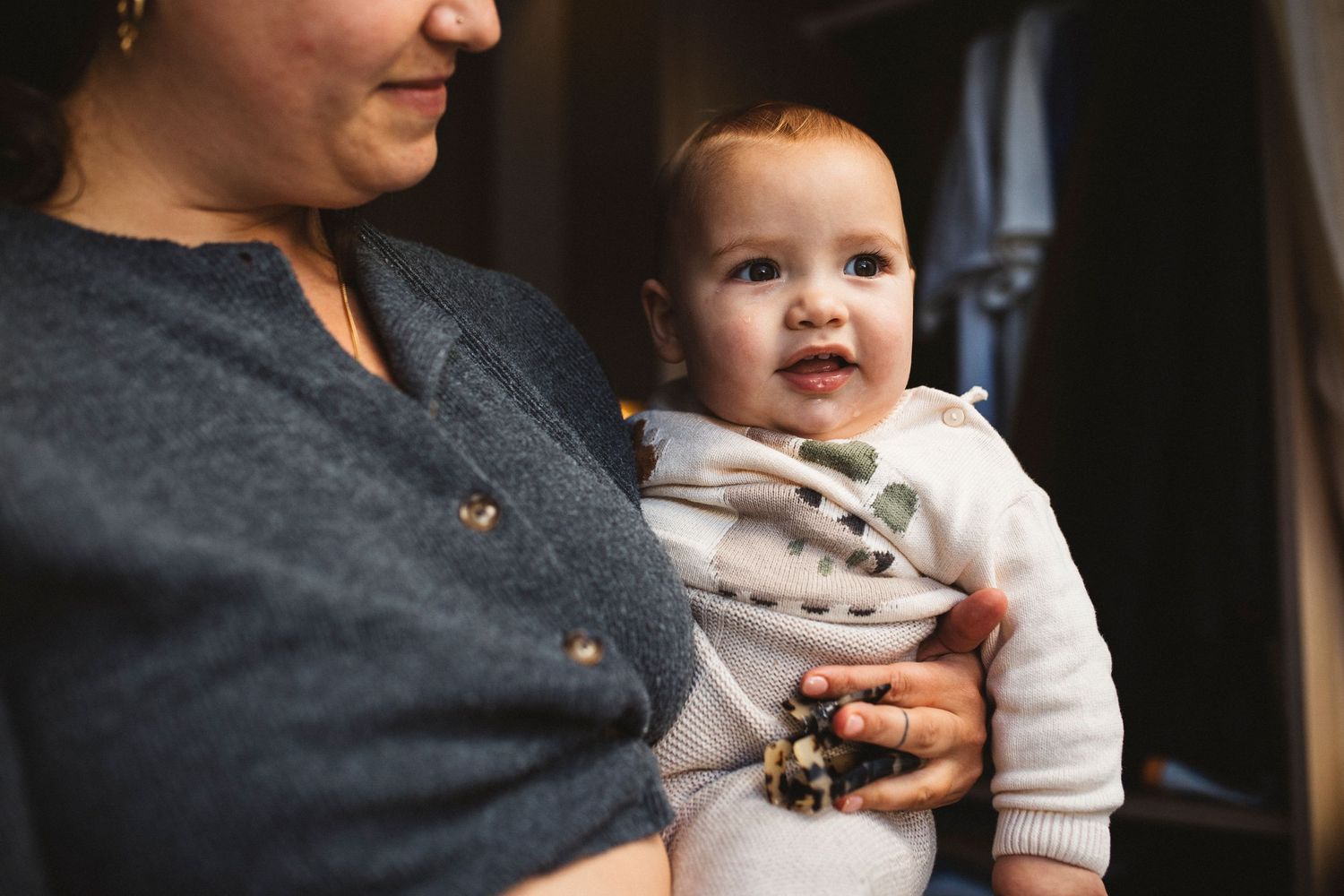 Close-up shot of a baby wearing a white sweater being held by someone in a dark gray button-up cardigan.