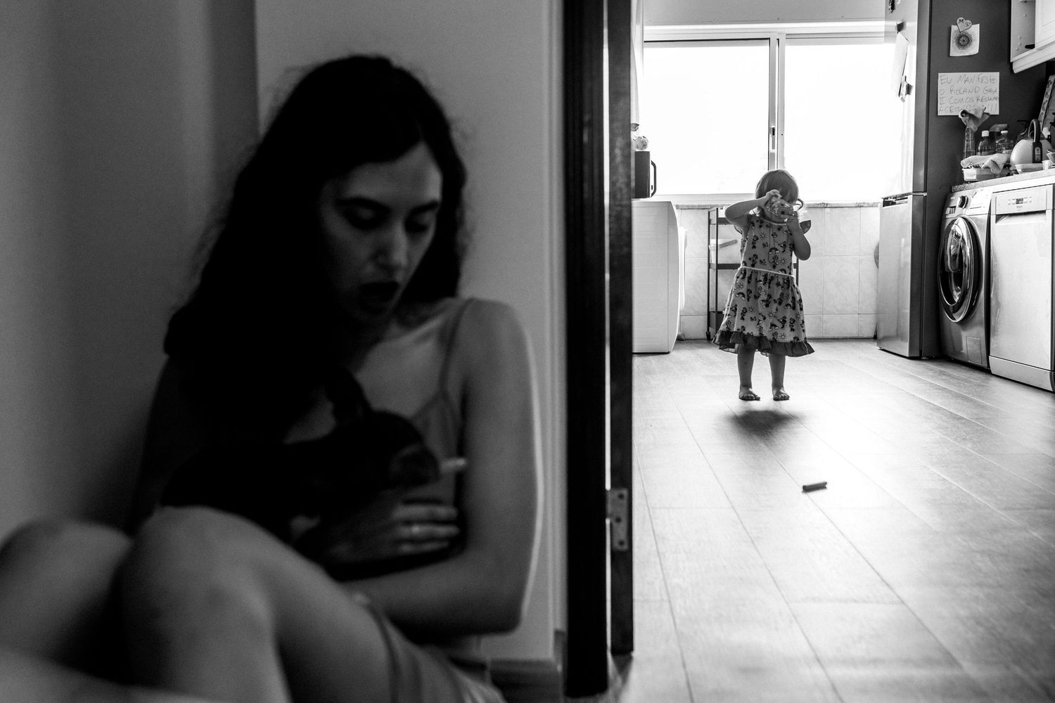 A black and white photograph showing a contrast between someone with a cat in shadows and a figure in a doorway.