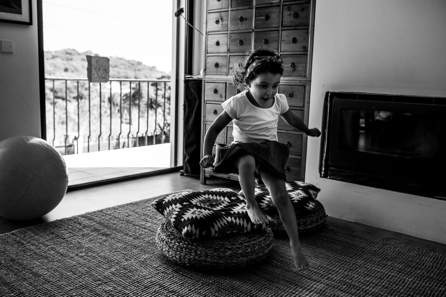A person sits on an indoor exercise ball beside a large basket filled with blankets in a monochrome photo.