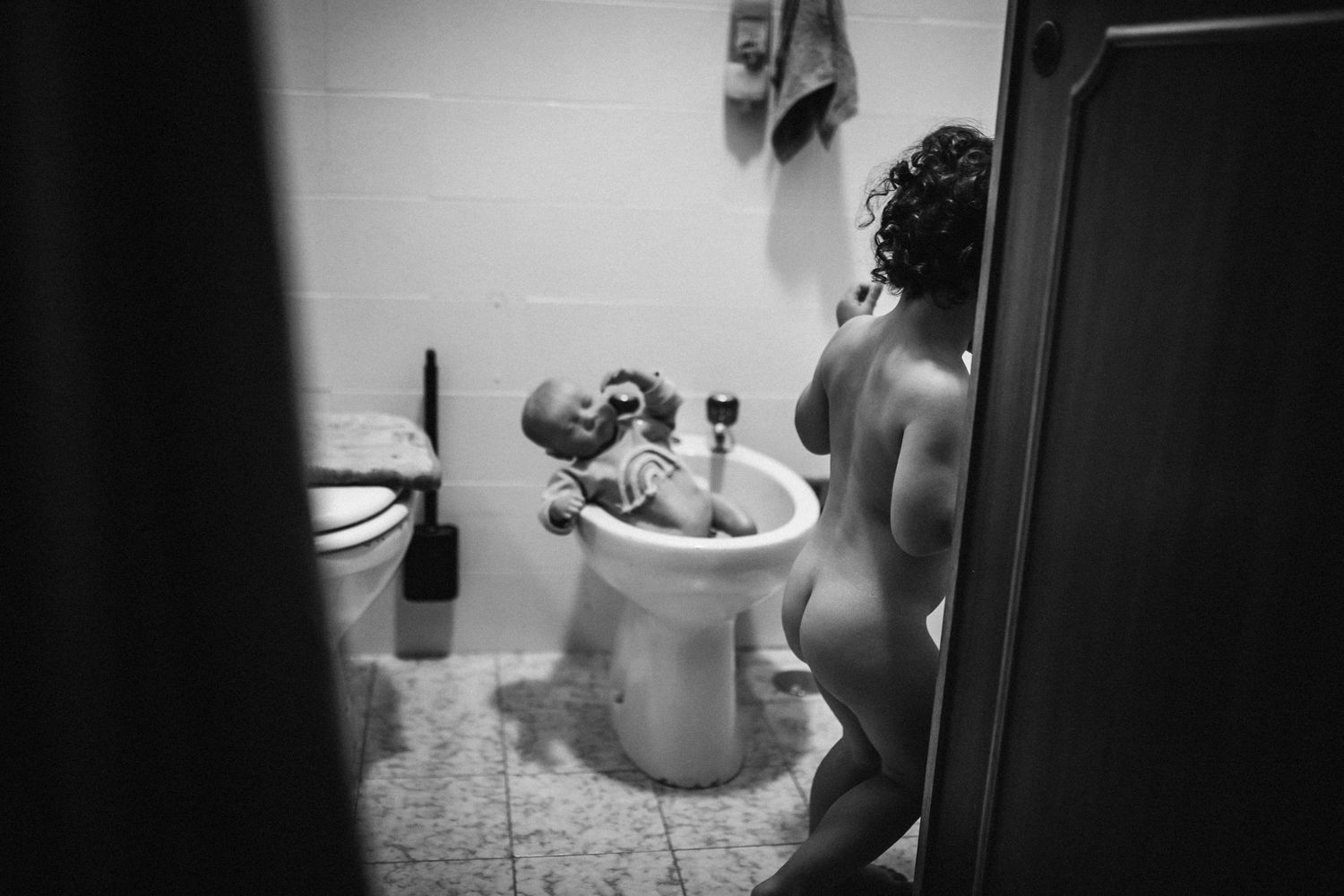 Black and white photograph of parent bathing infant in bathroom sink while standing.