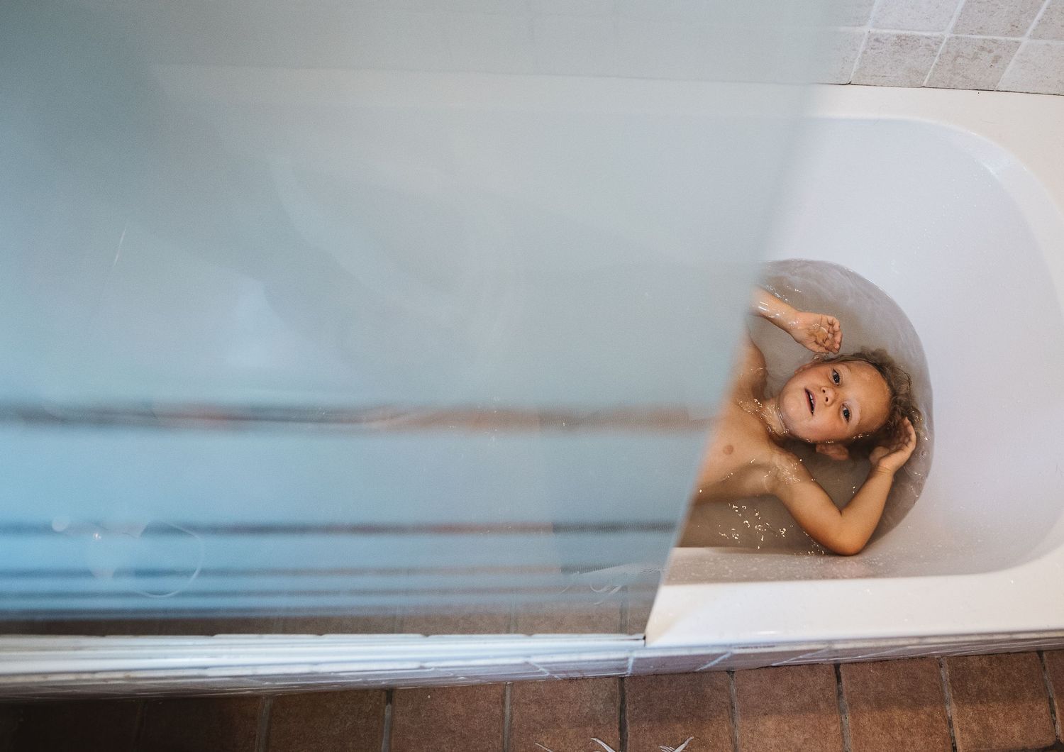 The silhouette of a person sits peacefully in a white bathtub with dreamy blue lighting.