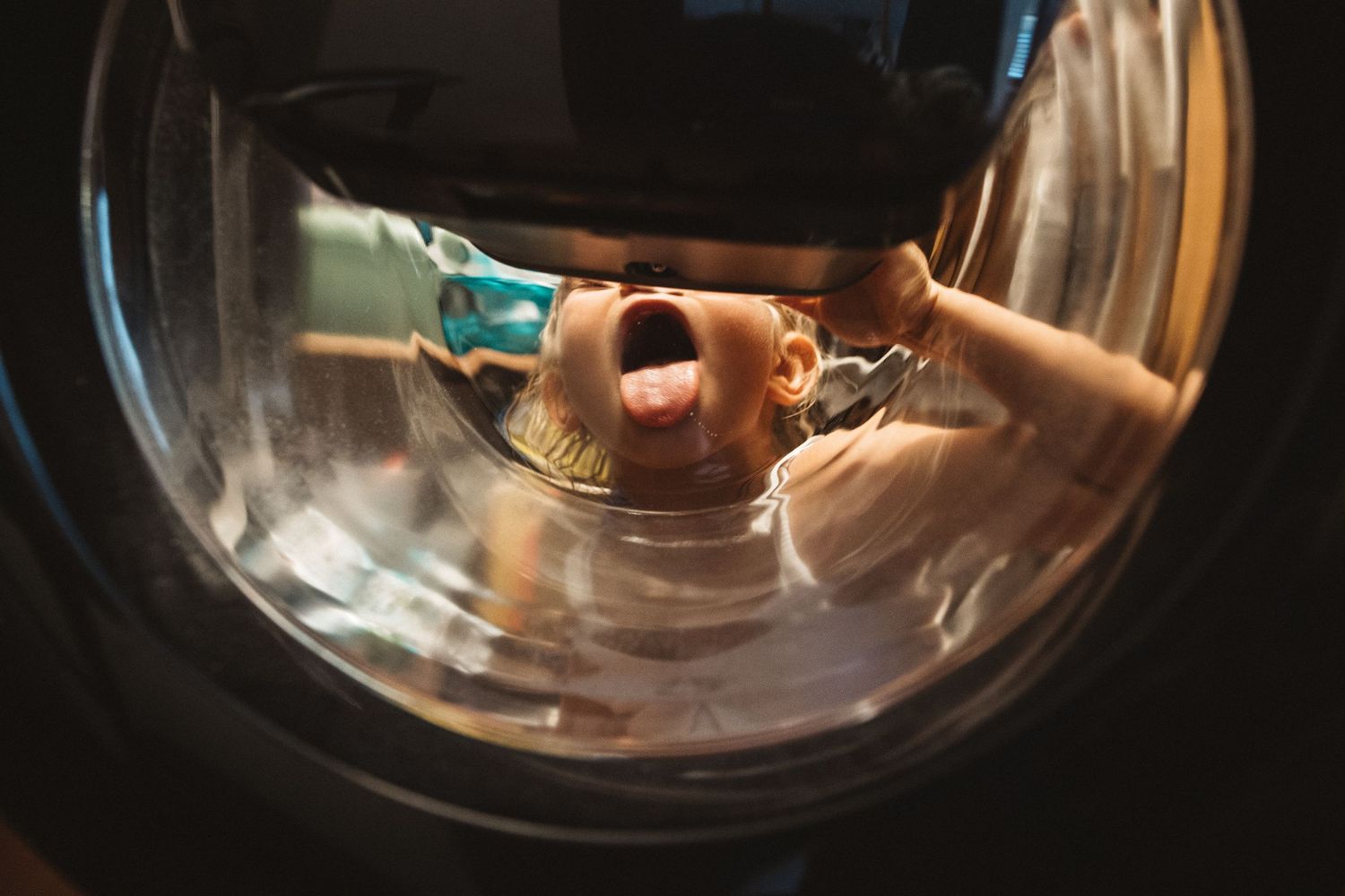 A view through a circular washing machine window showing hands loading laundry.