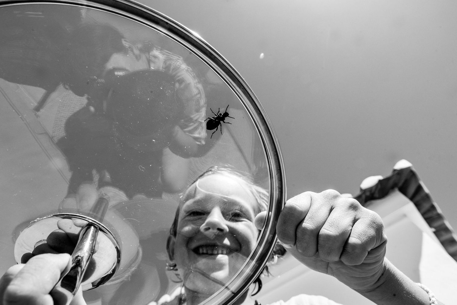A smiling person reflected in a circular mirror while wielding tools outdoors in black and white photography.