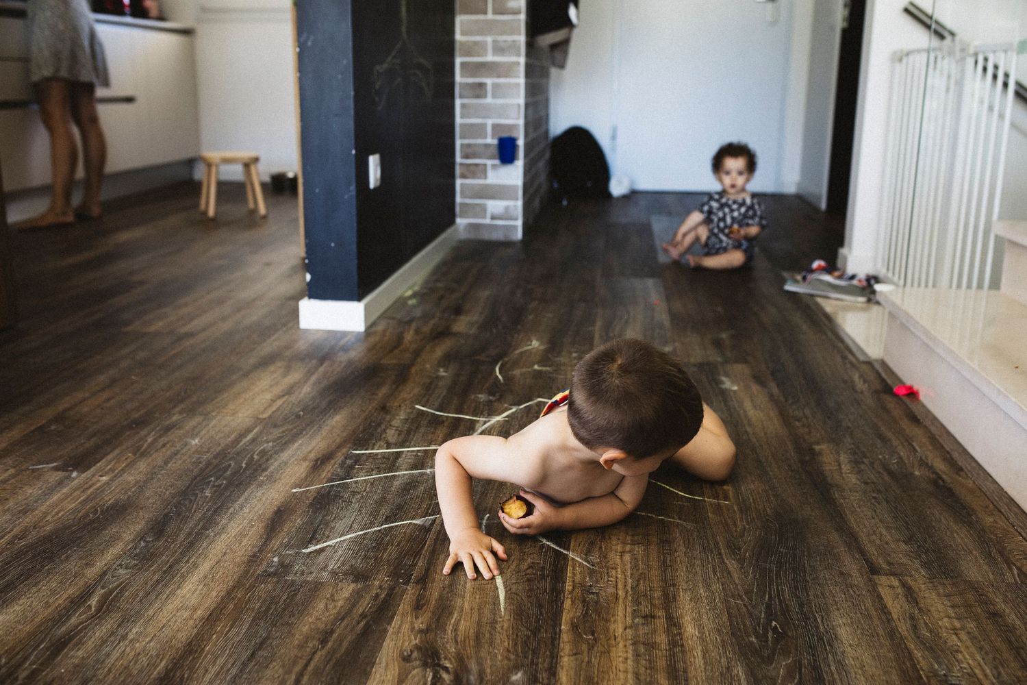 Children drawing with chalk on a dark hardwood floor inside a modern home with white walls.