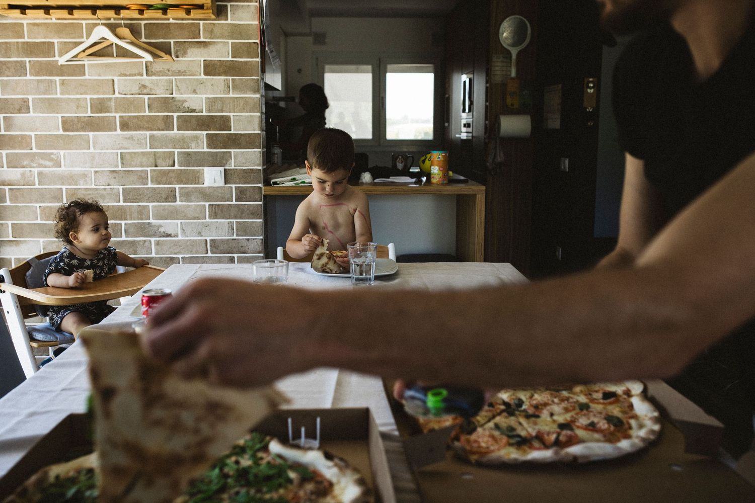 Family enjoying homemade pizza together at wooden dining table with brick wall backdrop in cozy kitchen setting.