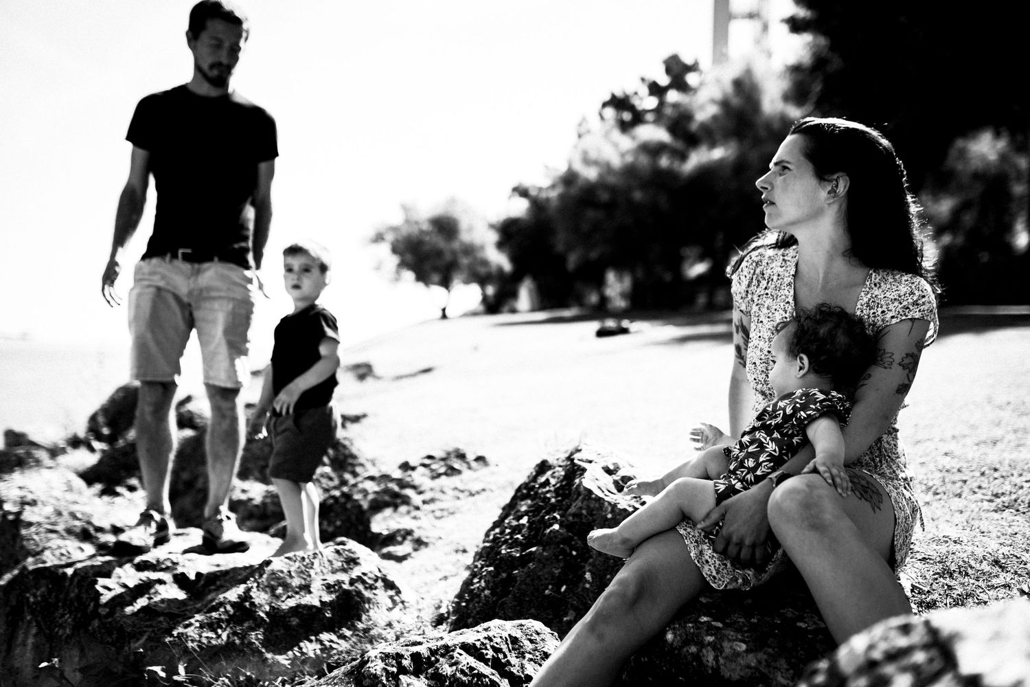 Black and white photo of people enjoying a sunny day by the water while sitting on rocky shoreline.