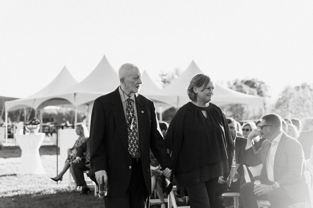 A vintage black and white photo of guests mingling at an outdoor event with white tents in the background.
