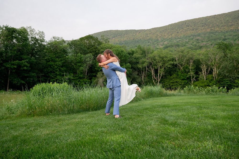 A couple shares a romantic twirling dance in a lush green meadow with mountains and trees in the background.