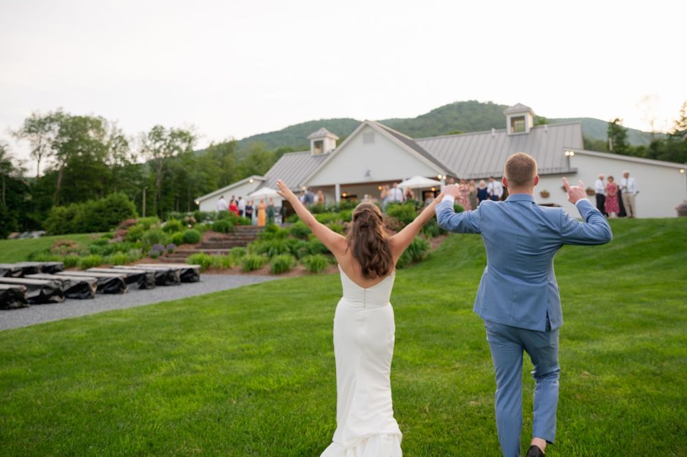 Wedding couple performs basketball celebration dance in matching blue and white outfits on grassy hillside lawn.