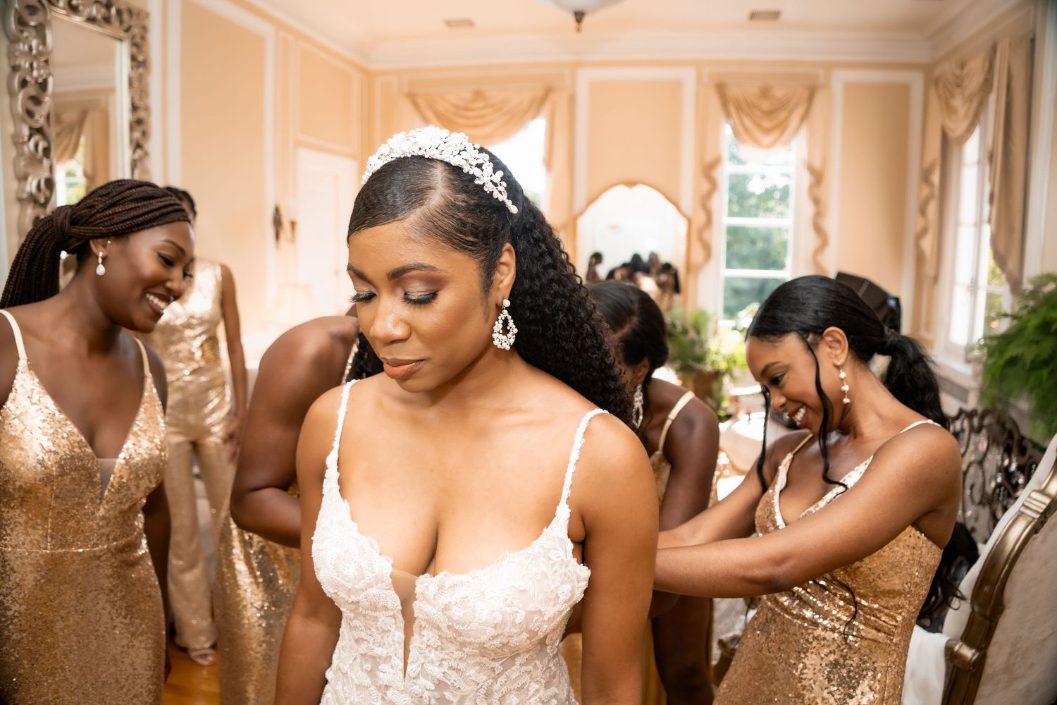 A group wearing sparkling gold bridesmaid dresses help prepare a bride in an elegant white wedding gown.