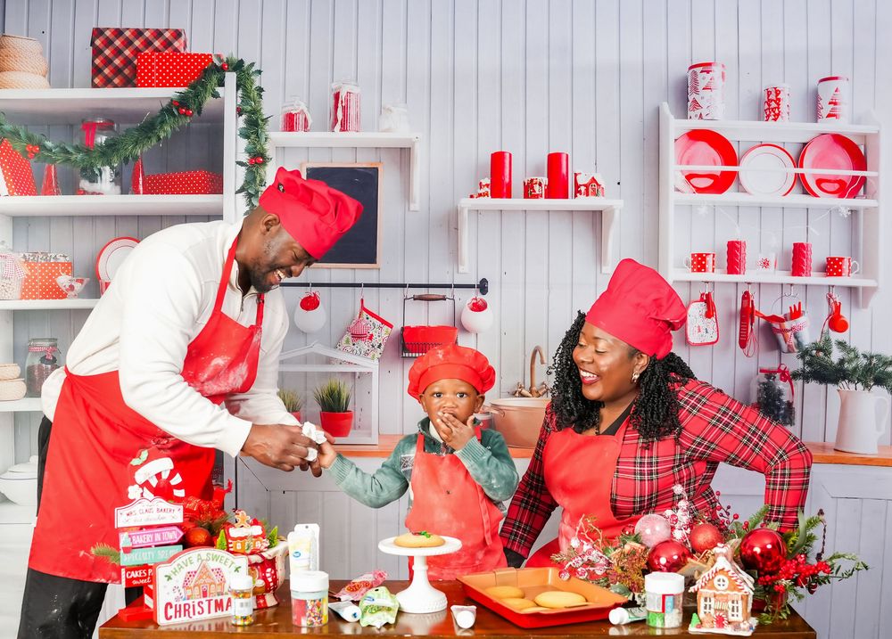 Five chefs in red holiday attire work together preparing festive treats and desserts in a bright kitchen setting.