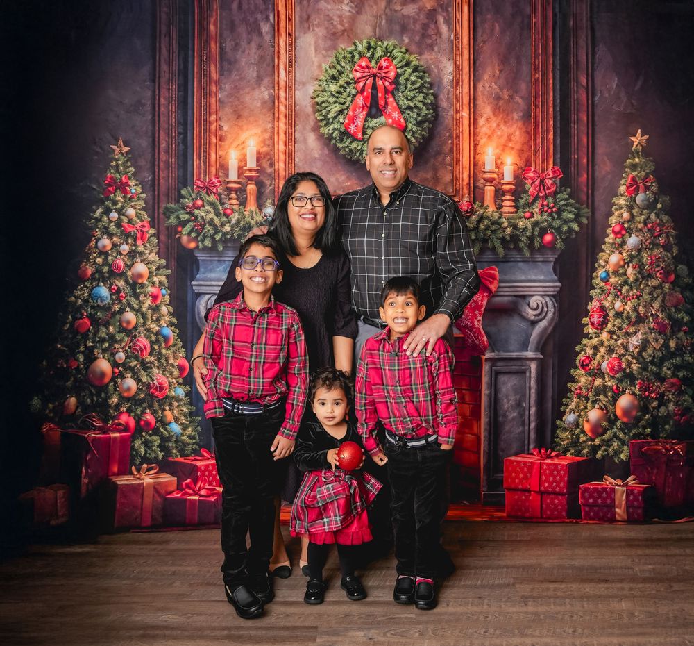 Christmas family portrait session with people in coordinating red plaid outfits posing in front of decorated trees and fireplace.