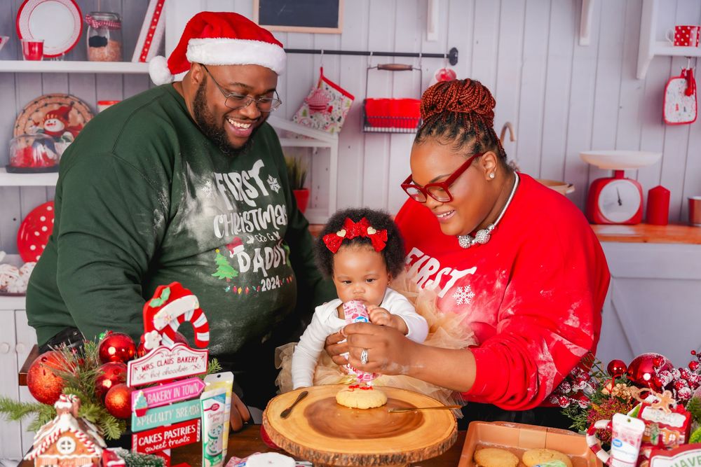 A family in Christmas attire decorates cookies together in a festive red and white kitchen setting during the holidays.