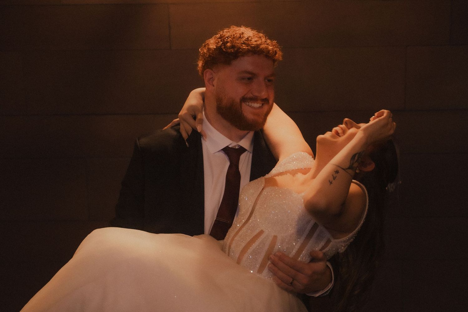 A wedding couple dances & laughs together in a romantic moment captured in warm dramatic lighting