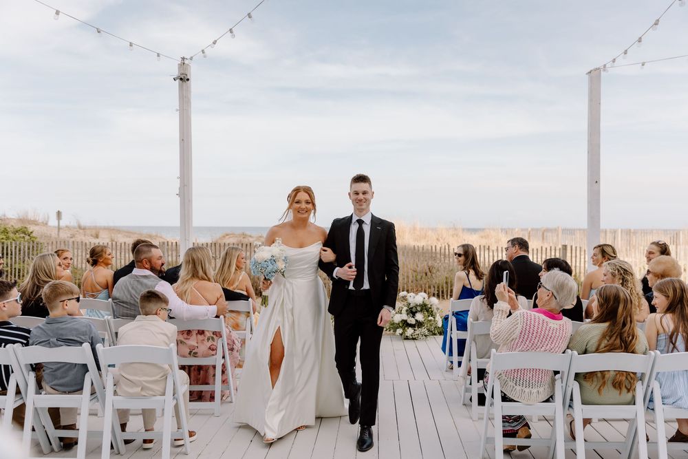 An outdoor wedding ceremony takes place at a scenic desert venue with white chairs and string lights overhead.