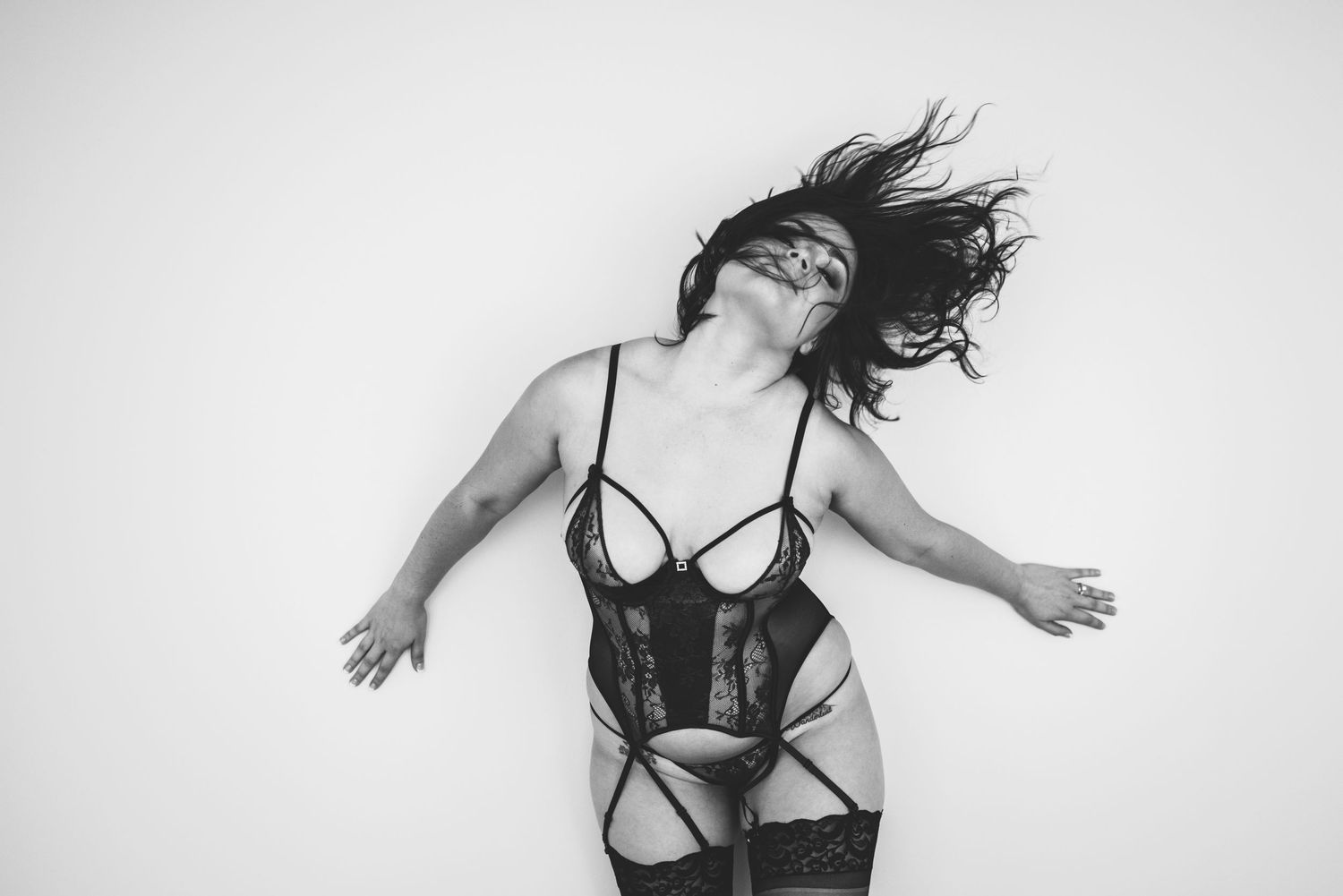 Black and white photo of person in lingerie lying on floor with hair in motion, expressing dynamic movement.