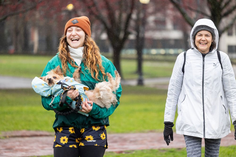 Two people enjoy a walk through a park with winter trees in the background on an overcast day.