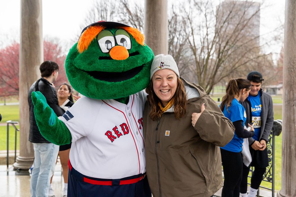 Boston Red Sox mascot Wally the Green Monster poses in his white jersey with a companion outdoors during a team event.