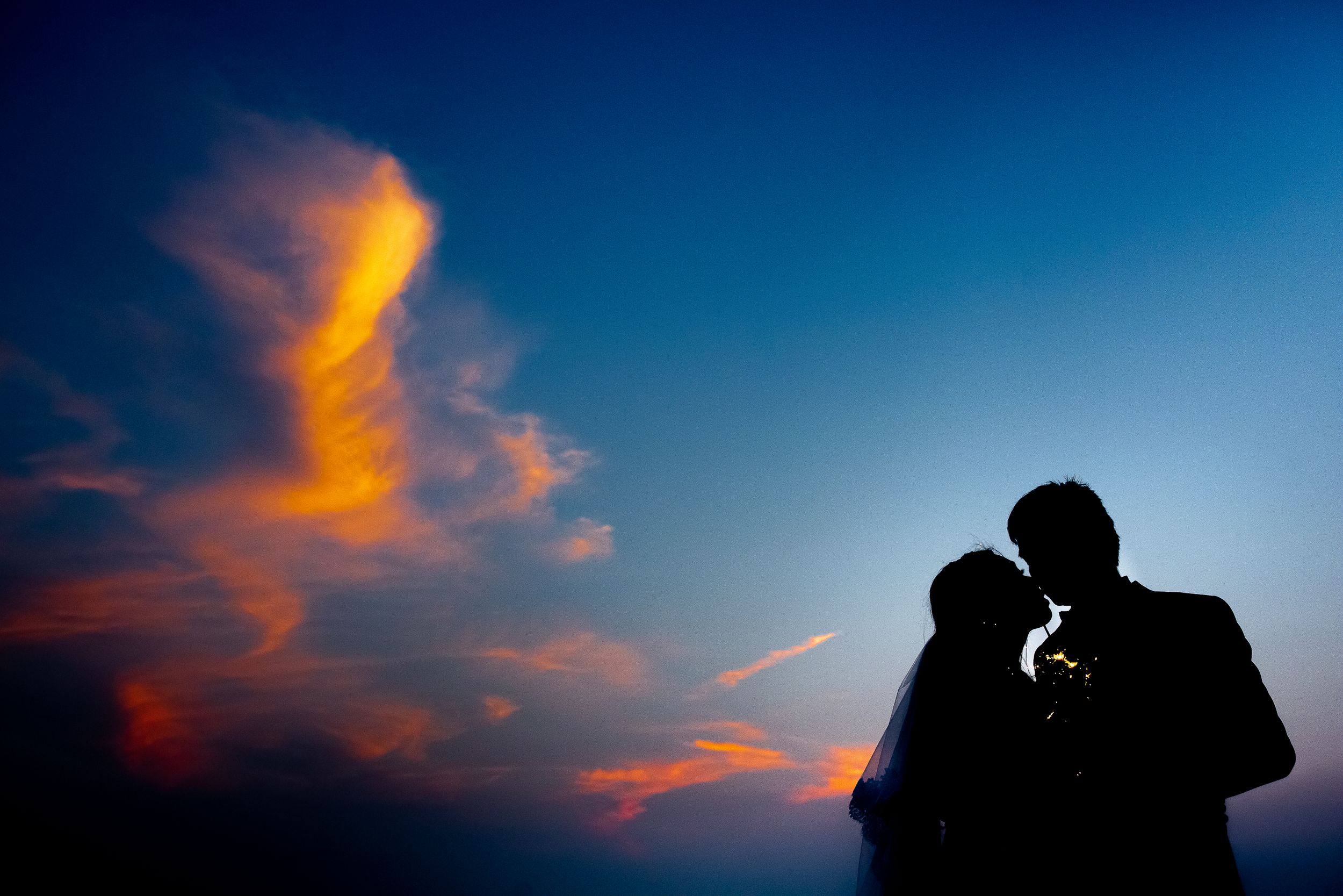 Romantic silhouette of a couple against a dramatic sunset sky with orange clouds.