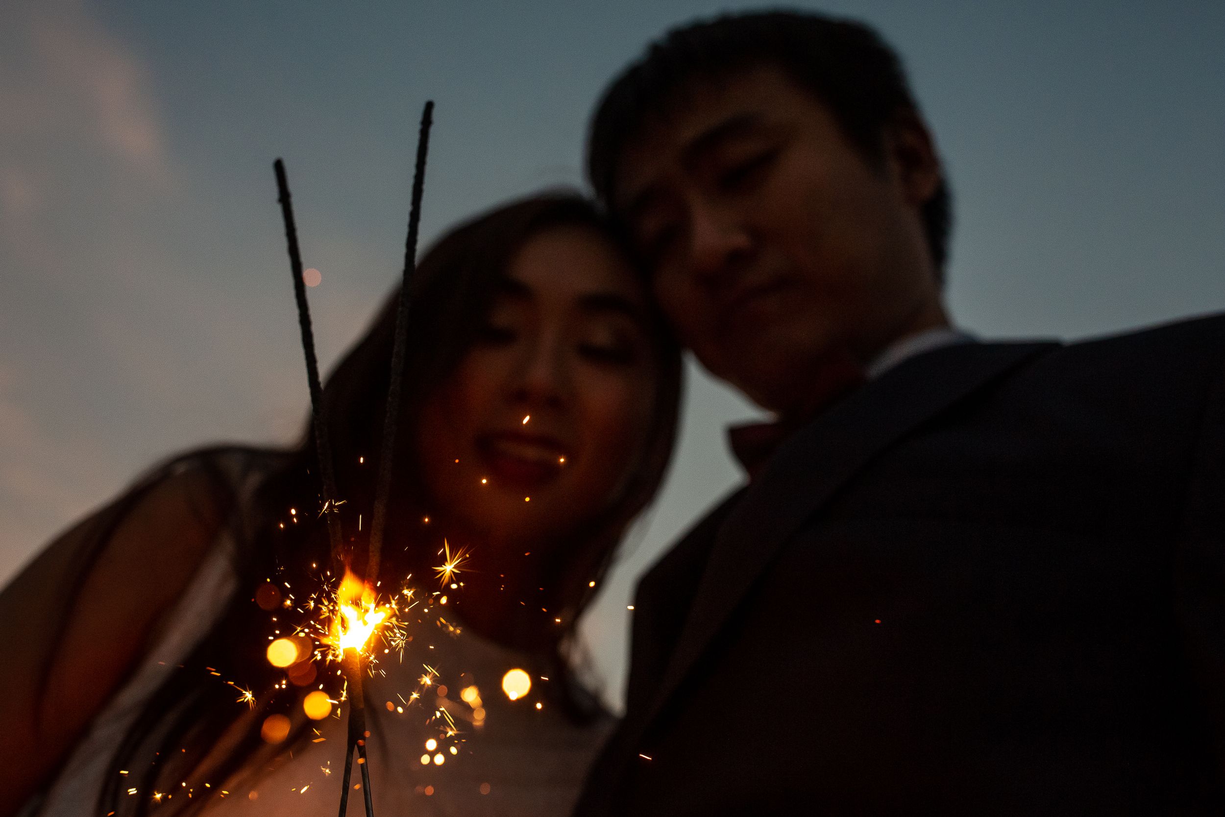 Couple holding sparklers at dusk creating a magical wedding moment.