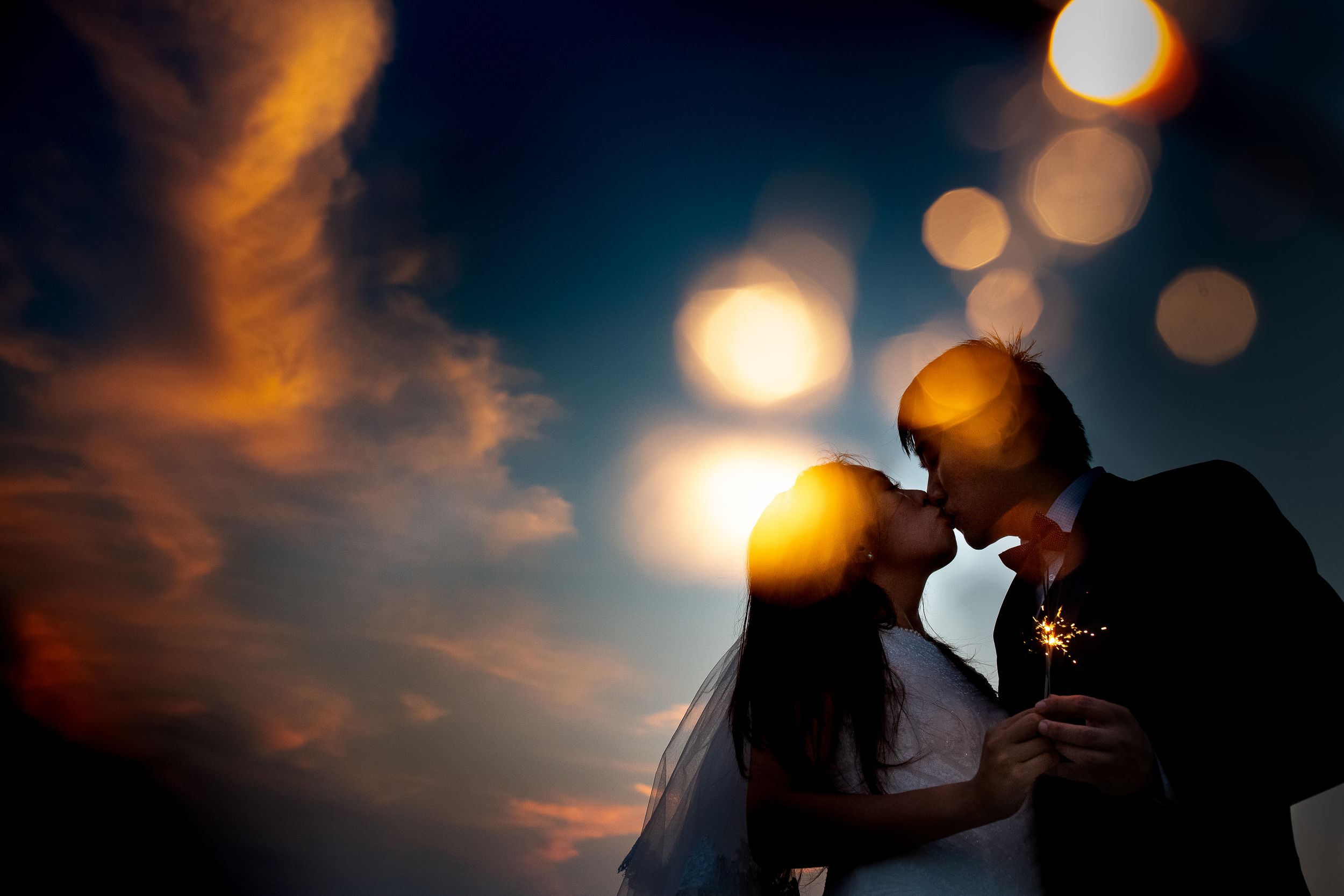 Silhouetted couple sharing an intimate moment against a bokeh sunset background.