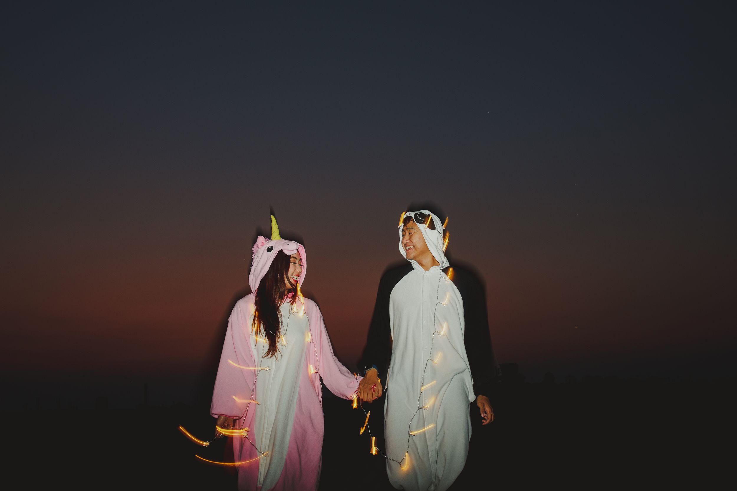 Two people in whimsical unicorn costumes standing together at twilight.