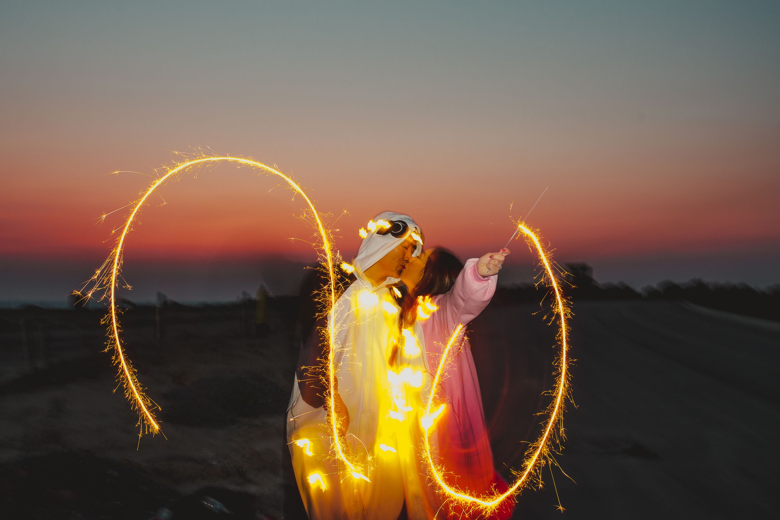 Couple in costumes creating light trails with sparklers during sunset.