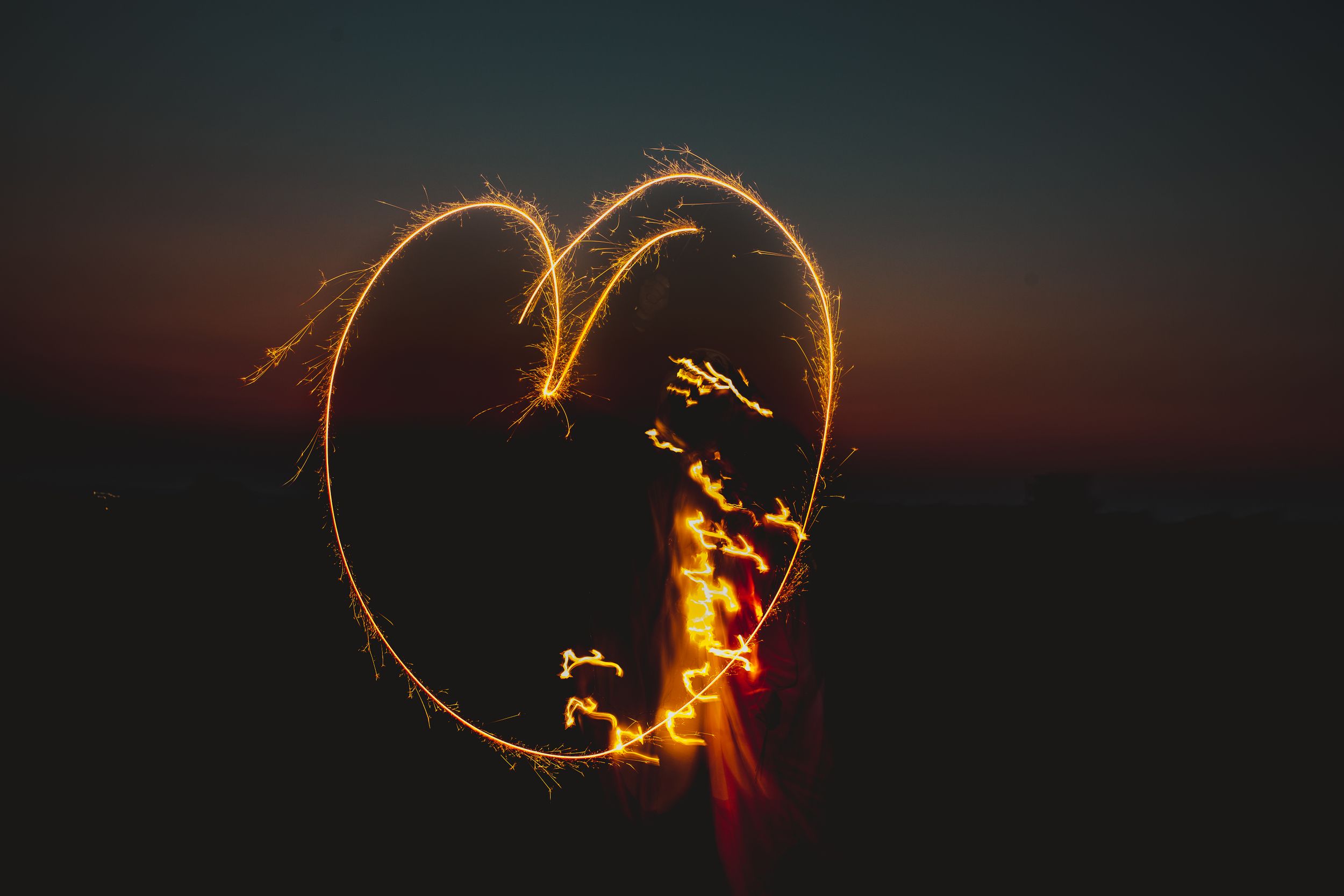 Heart shape drawn with sparklers against a dusky sunset sky.