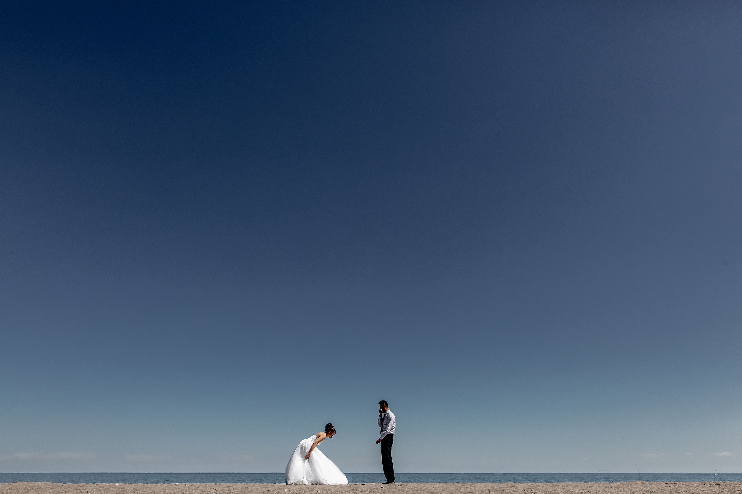 Minimalist beach wedding photo with couple against vast blue sky and white sand.