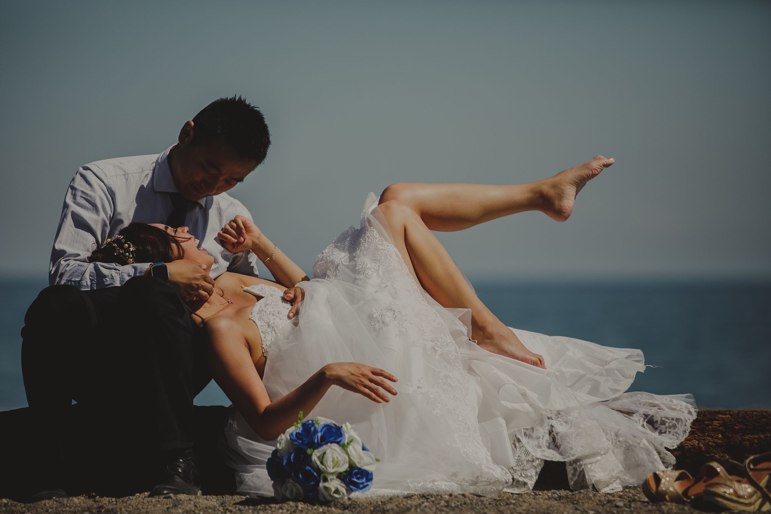 Relaxed seaside wedding portrait showing couple's feet and dress details against ocean backdrop.