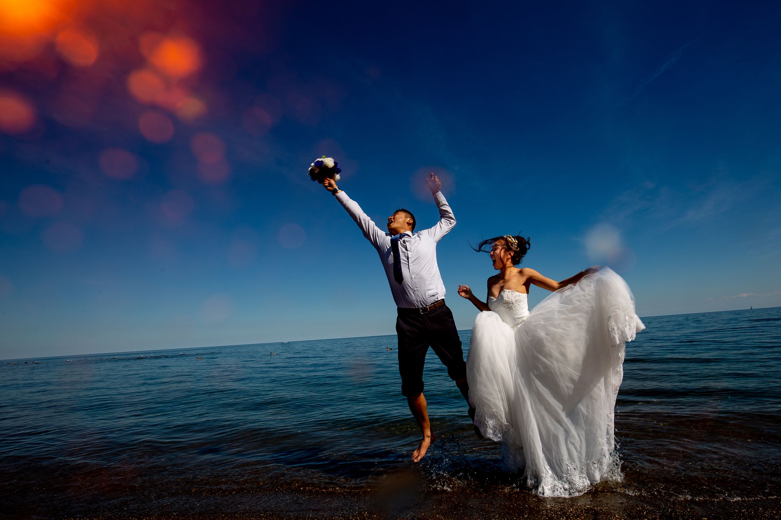 Energetic couple celebrates in ocean water during sunset wedding photoshoot.