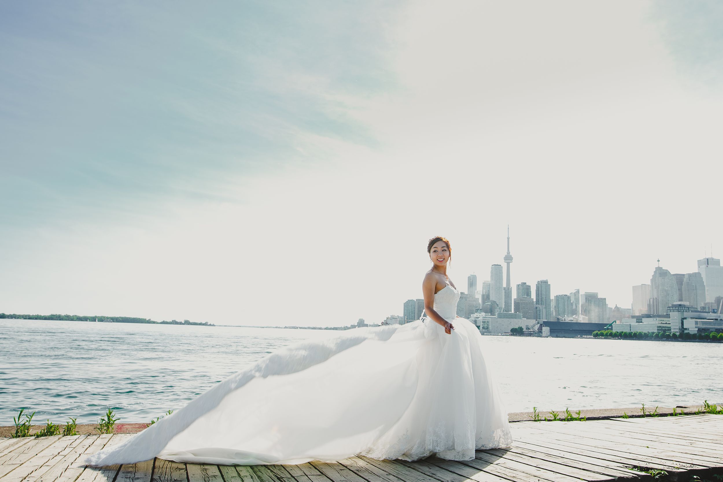Bride in flowing white gown poses against Toronto harbor skyline.